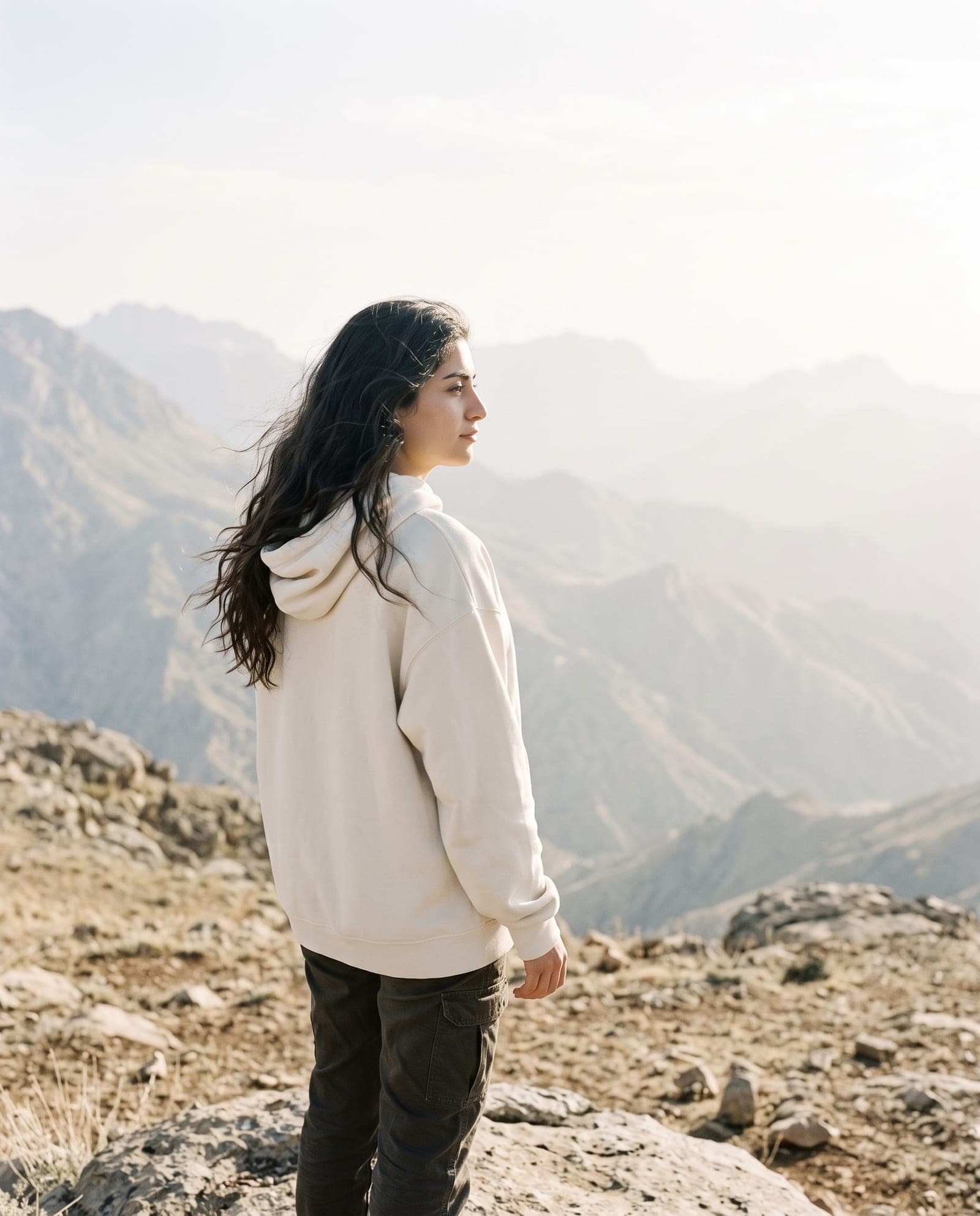 A woman in a bone-colored heavyweight hoodie looking across a hazy mountain plateau